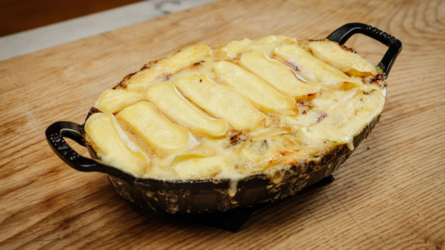 Tartiflette in a cast iron pan on a wooden table recipe poster image